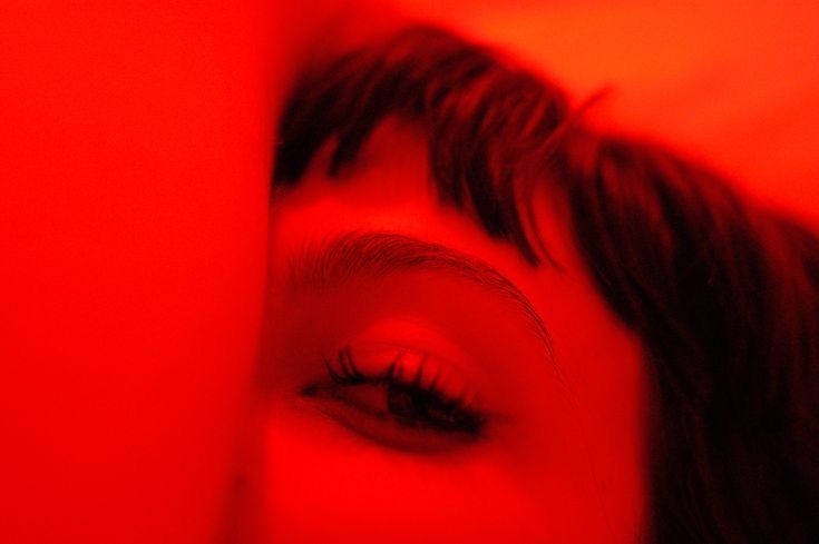 Gros plan sur le regard d’une femme à frange, baigné de lumière rouge