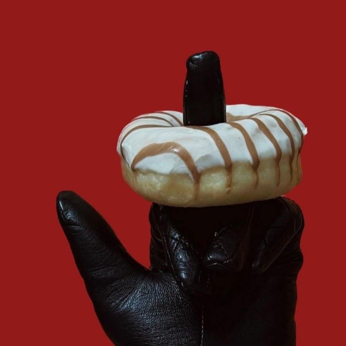 Main gantée de cuir noir avec un donut glacé enfilé sur un doigt, sur fond rouge