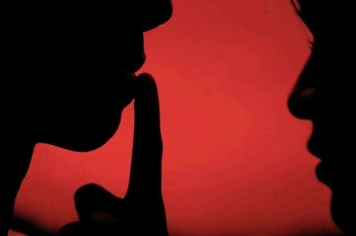 Silhouettes de deux visages de profil sur fond rouge, l'un faisant signe de se taire