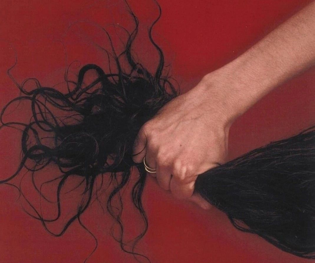 Une main qui serre une longue mèche de cheveux noirs sur fond rouge