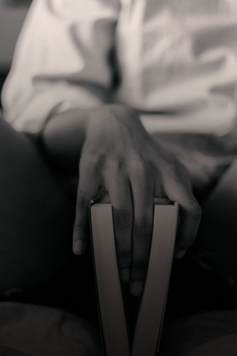 Mains d'une personne en chemise blanche posées sur un livre fermé, en noir et blanc